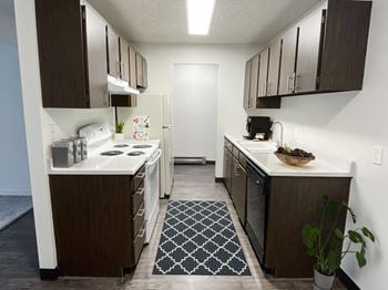 A kitchen with wooden cabinets and white appliances and a blue and white rug